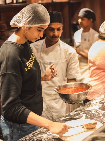 One of our chefs guides a guest as she spreads the San Marzano tomato sauce on her dough. We're there to help you make the perfect pie.