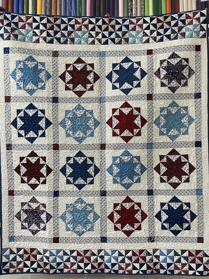 A classic Lone Star quilt in patriotic red, white, and blue, with a pinwheel border. Our quilting adds texture to the open spaces.