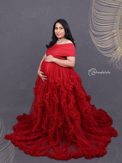 A lovely studio portrait of a mother-to-be in a red ruffled gown, holding a basket of flowers.