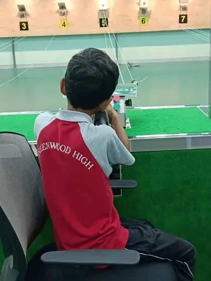 A student from Greenwoods High takes aim from a seated position, using an ergonomic chair for support. This setup helps isolate the movements of aiming and trigger control.