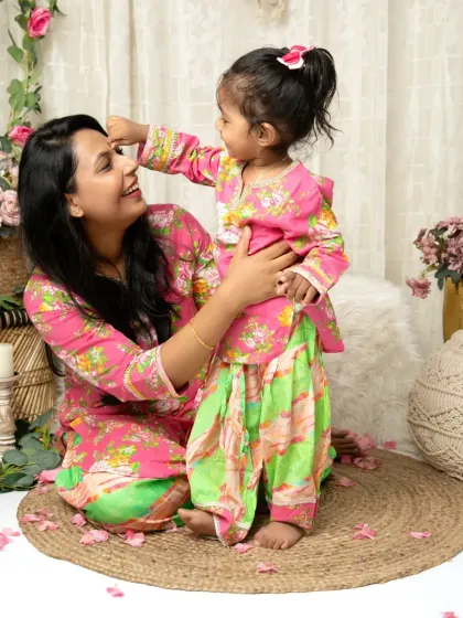 A playful moment where a little girl in a traditional outfit puts a bindi on her mother's forehead.