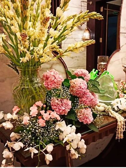 An elegant console table arrangement. A large vase of tuberoses is paired with a beautiful bouquet of pink hydrangeas and white orchids, perfect for a welcoming entryway.