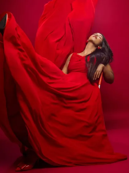 A dramatic, artistic shot with a flowing red dress. The model is enveloped in fabric, creating a powerful and abstract fashion image.