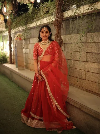 A full-length view of our client in a stunning red lehenga, rented for her sister's wedding. The delicate embroidery and sheer dupatta create a classic, timeless look perfect for any wedding celebration.