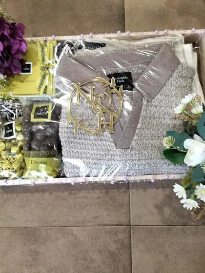 This trousseau gift box is designed for apparel, featuring a folded sweater alongside gourmet chocolates. We ensure clothing items are packed neatly and presented attractively, complete with a personalized monogram and floral details.