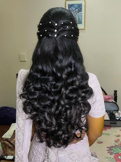 A half-up hairstyle with tight, bouncy curls, featuring a criss-cross pattern at the crown adorned with pearls.