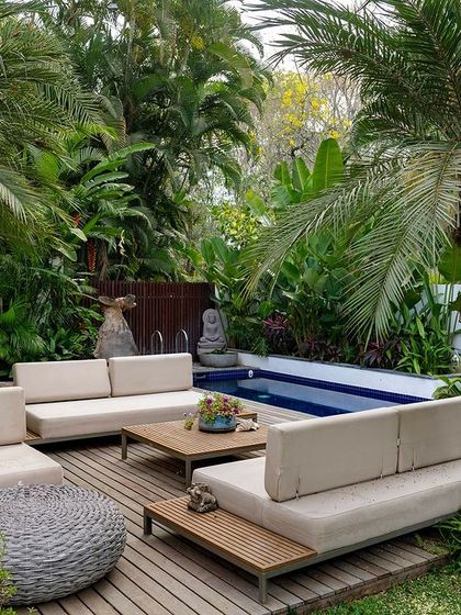 A poolside deck with modern outdoor furniture, surrounded by palm trees and tropical foliage. This space is designed as a private oasis for relaxation and socializing, blending the comfort of a lounge with the beauty of a garden.