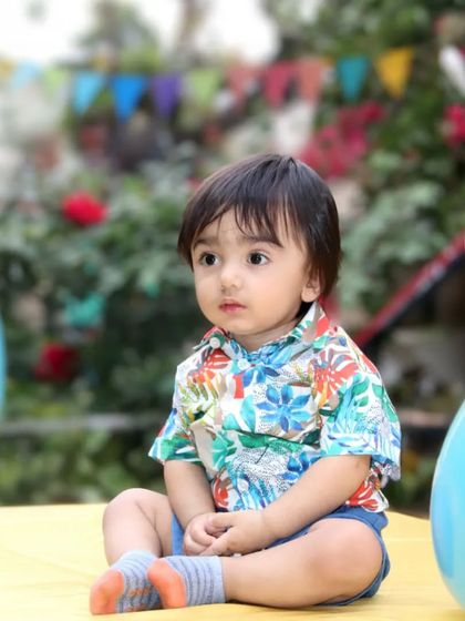 A beautiful outdoor portrait of a toddler sitting peacefully amidst blurred balloons and greenery.