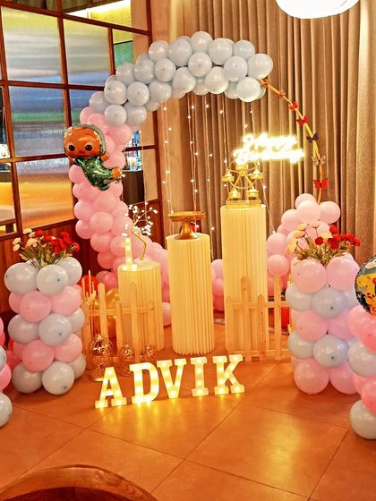 A colorful Cocomelon themed first birthday party. This setup features character foil balloons, a pastel balloon arch, a small white picket fence, and light-up letters for the child's name, creating a playful atmosphere.
