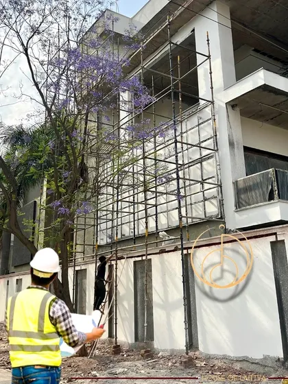 An architect in a hard hat reviews plans on-site, with the building's facade and scaffolding in the background, representing our hands-on project management.