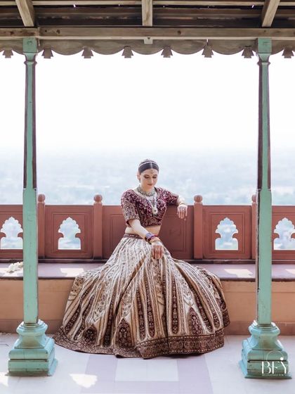 A full-length portrait of a bride sitting on a balcony, her grand lehenga spread beautifully.
