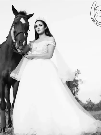 A timeless black and white portrait of a model in a flowing white gown standing with her horse, creating a classic and elegant equestrian look.