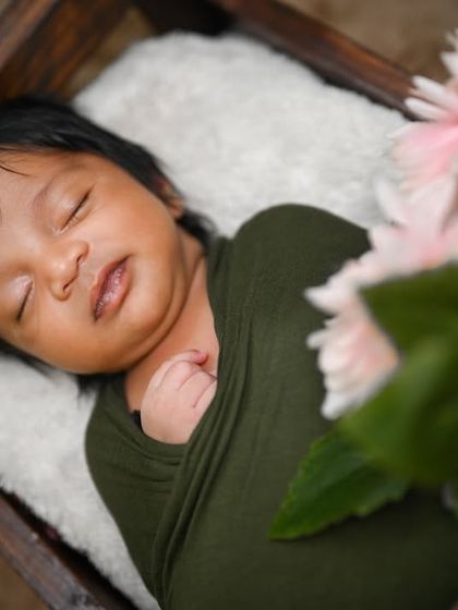 A close-up of a newborn wrapped in olive green, sleeping peacefully in a wooden crate.
