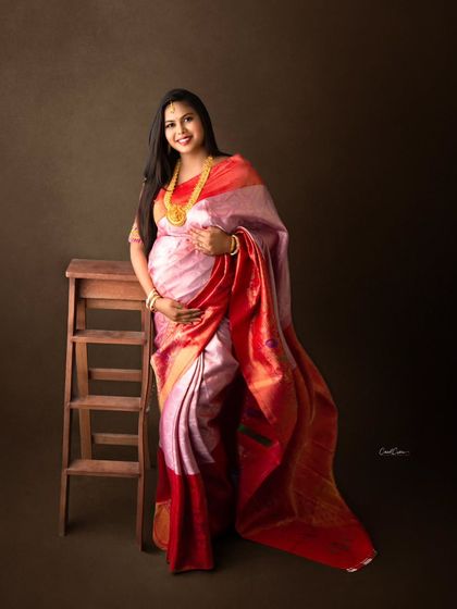 A classic portrait of a mom-to-be in a beautiful pink and red silk saree, accessorized with traditional gold jewelry.