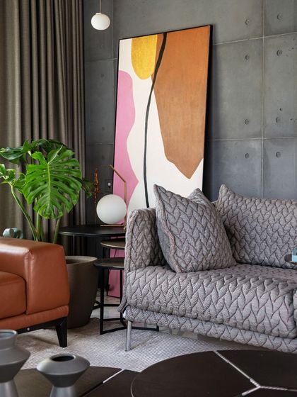 A detail shot of the living room seating, showing the combination of a patterned fabric sofa and a tan leather armchair. Abstract art and indoor plants add color and life to the sophisticated palette.