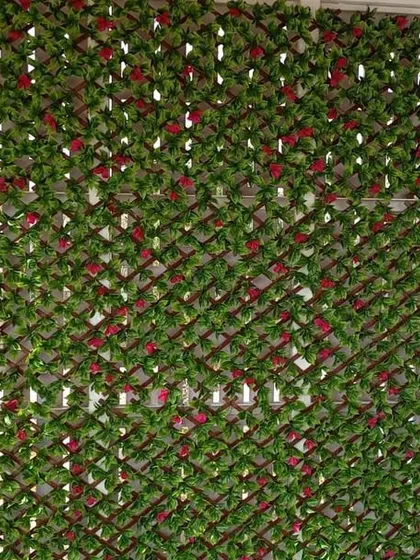 This expandable artificial leaf trellis, featuring red rose accents, is a quick and effective way to create a decorative privacy screen.