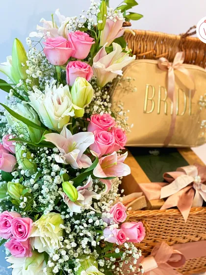 A close-up of our bride's essentials hamper, highlighting the lush arrangement of pink roses and lilies that accompanies the curated gifts.