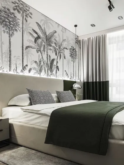 This bedroom features a striking black-and-white tropical mural, creating a dramatic and immersive atmosphere. The green bedspread and simple headboard complement the wallpaper perfectly.