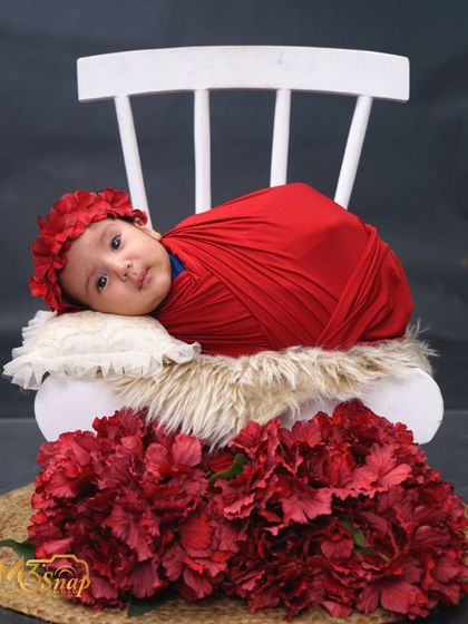 A beautiful portrait of an awake newborn wrapped in a vibrant red swaddle. Her curious eyes and the bold color make this a very striking image.