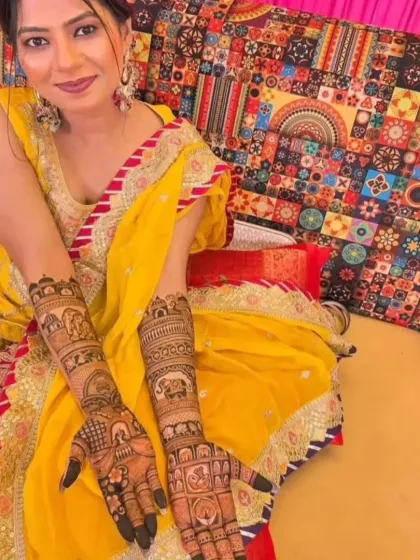 A happy bride posing with her intricate full-hand Rajasthani mehndi. The vibrant yellow of her outfit makes the dark henna stain pop.