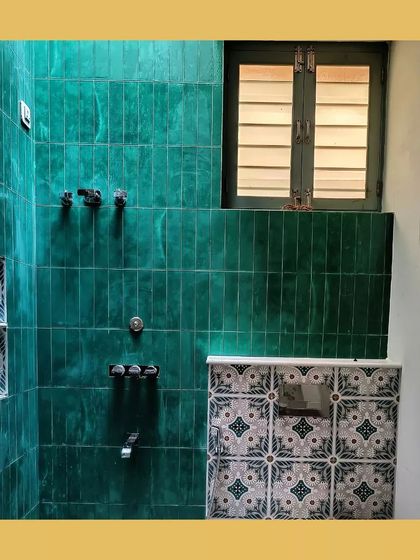 A bathroom featuring vibrant green handmade tiles, contrasted with traditional patterned tiles, all lit by a high window.