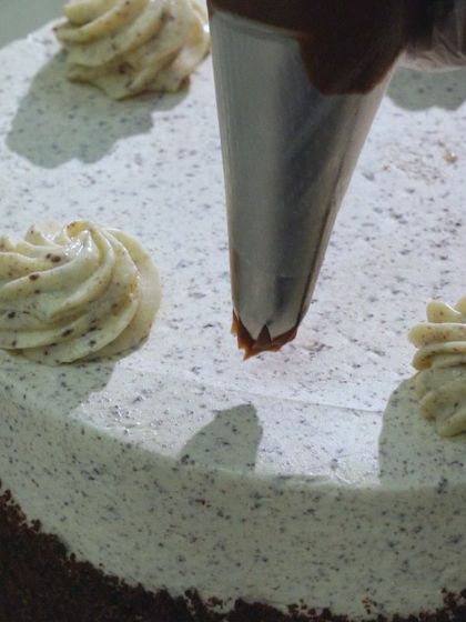 The final touches on the Cookie & Cream Cake. I pipe rosettes of chocolate ganache on top of the Oreo cream cheese frosting before adding the cookie garnish.