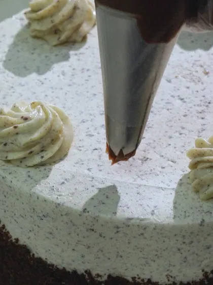 The final touches on the Cookie & Cream Cake. I pipe rosettes of chocolate ganache on top of the Oreo cream cheese frosting before adding the cookie garnish.