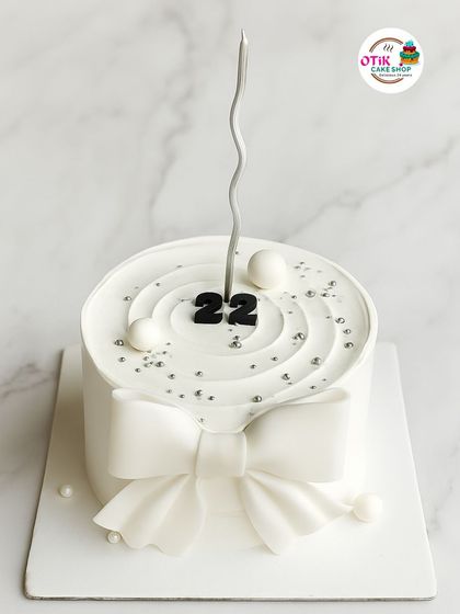 A minimalist masterpiece for a 22nd birthday. This all-white cake features a simple, elegant fondant bow and delicate silver pearl sprinkles for a look that is both modern and timeless.