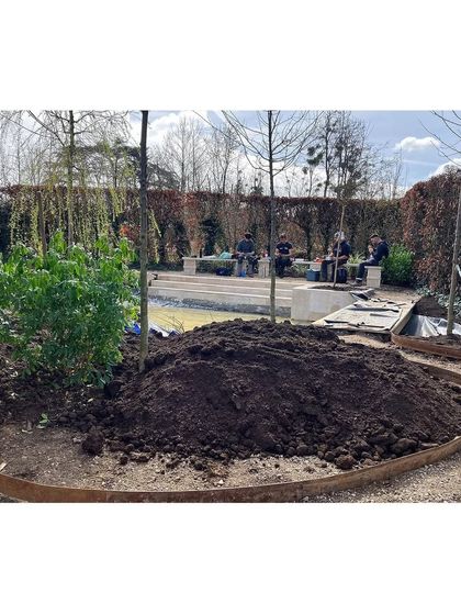 A large mound of rich soil is ready to be spread. Building a resilient garden starts from the ground up, with careful preparation of the soil to ensure a healthy foundation for the plant life to thrive.