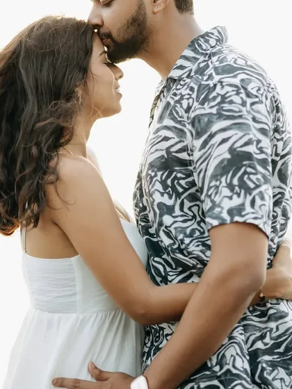 A simple, tender forehead kiss against the bright sky. This is a classic romantic couple portrait that focuses purely on the emotion between two people.