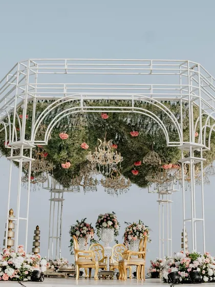 A closer look at the mandap's canopy, which is a dense ceiling of greenery and pink flowers, with dozens of small chandeliers hanging down to create a magical, twinkling effect.