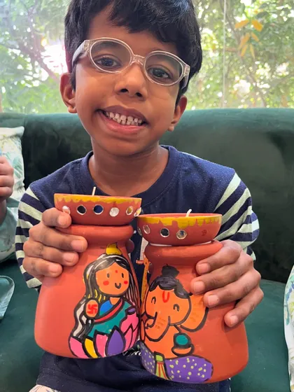 This young artist proudly displays the adorable Lakshmi-Ganesha diya holders he painted.