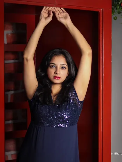 A full-body shot with arms raised, creating a strong, elegant silhouette against the red backdrop.