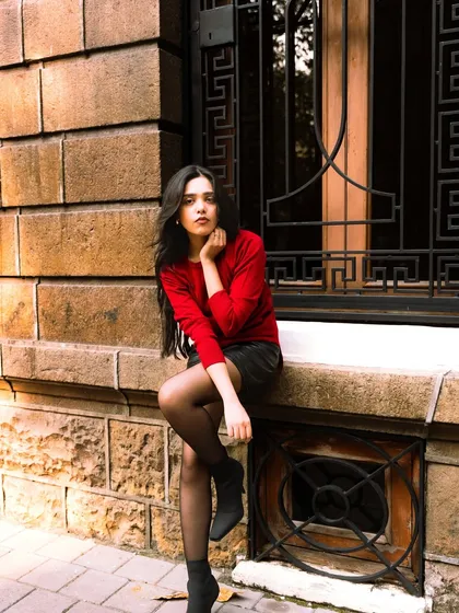A chic, European-style street portrait. The combination of the red sweater, stone architecture, and elegant pose creates a sophisticated look.