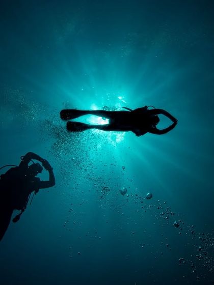The sun's rays pierce the surface, creating a beautiful silhouette of two divers exploring the depths in Sipadan.