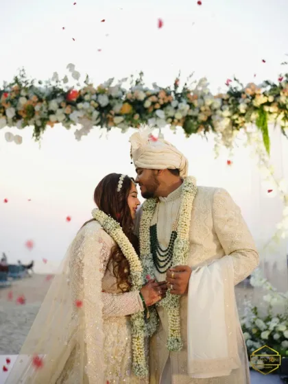 An intimate moment between the couple under a floral arch. The bride's makeup is soft and romantic, perfect for this dreamy beachside setting.