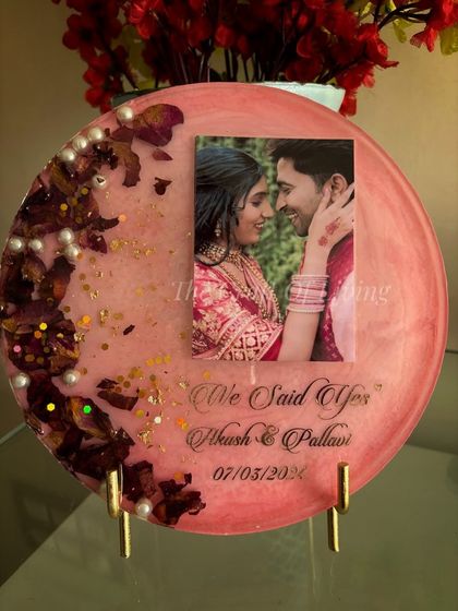 A round decorative plate in a soft pink resin, perfect for preserving engagement flowers. This design features the couple's photo, their names, and the phrase "We Said Yes" to commemorate the special occasion. The preserved petals are arranged in a crescent shape, accented with pearls and gold flakes.
