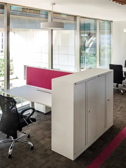 Workstations at the Stainless Steel Office are designed for efficiency with views overlooking the landscaped courtyard. Each workstation cluster is defined by a specific color, such as this vibrant pink, to delineate different teams or departments.