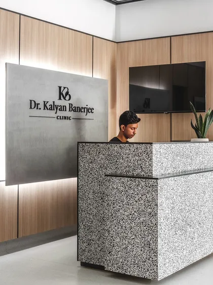 A closer view of the reception at Dr. Banerjee's Clinic. The custom-designed desk, made from black and white quartz, serves as an elegant centerpiece, while the backlit signage and wood paneling establish a professional and welcoming atmosphere.