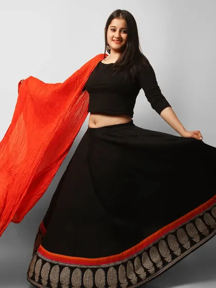 A model in a black lehenga with a contrasting red dupatta. The pose creates a sense of movement and joy, making it a great image for a festive campaign.