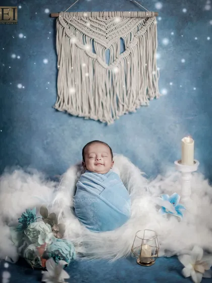 A baby boy wrapped in a cozy blue swaddle, captured with a sweet, fleeting smile. Our dreamy blue setup with soft clouds and gentle lighting creates a peaceful and angelic atmosphere.