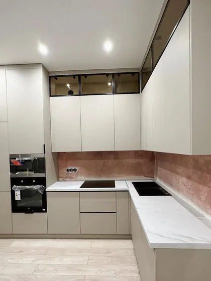 A U-shaped kitchen with matte off-white cabinets and a striking rose-gold or copper-toned backsplash. The design includes smoked glass upper cabinets and integrated appliances for a sophisticated look.