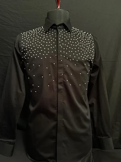 A black designer shirt featuring a cascade of white pearls across the shoulders and chest. This piece offers a look of modern luxury and standout elegance.