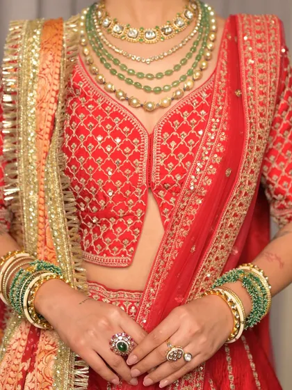 A detailed shot focusing on the exquisite bridal jewelry and the rich colors of the lehenga. The makeup is designed to complement these elements, with a neutral palette that allows the accessories to shine.