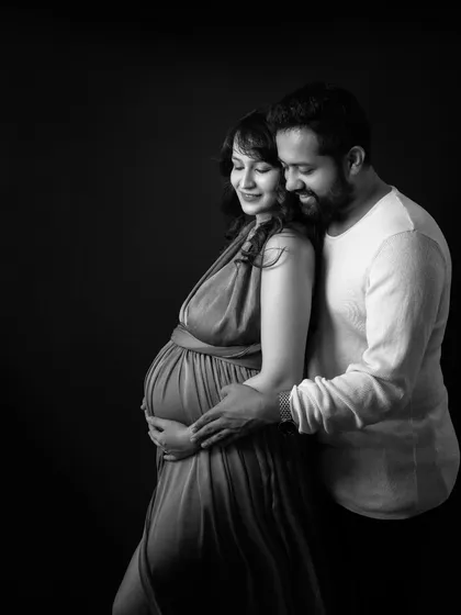 Whispers of love in black and white. This intimate portrait uses a dark background to draw all attention to the couple's tender embrace and the beautiful shape of the baby bump they cradle together.