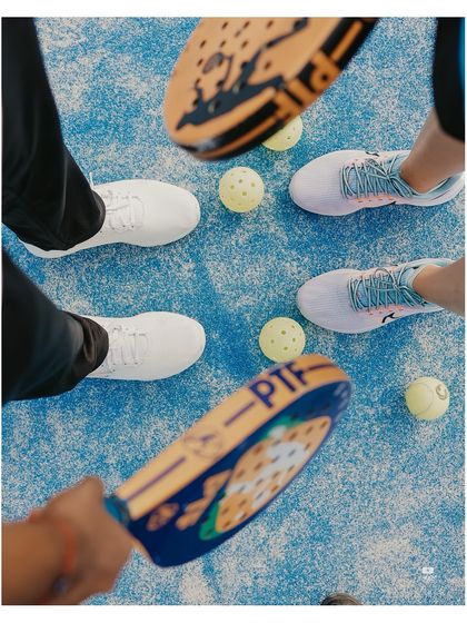 A unique top-down perspective of the couple's shoes, rackets, and Padel balls, creating a graphic and interesting composition.