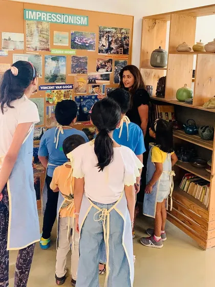 An instructor gathers students to discuss the Impressionist movement, using visual aids and examples to explain the concepts of light and color before they begin their Van Gogh inspired paintings.