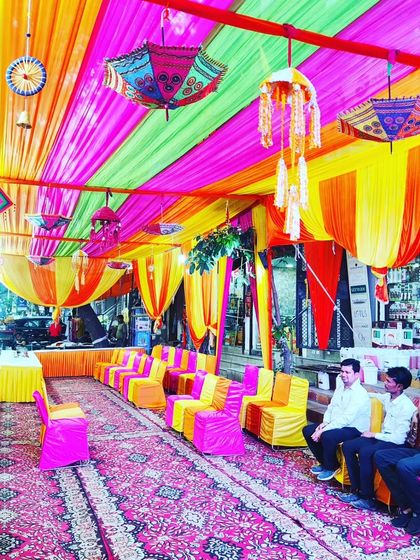 A lively street-side tent for a Mehendi function, filled with colourful drapes, umbrellas, and seating for guests.