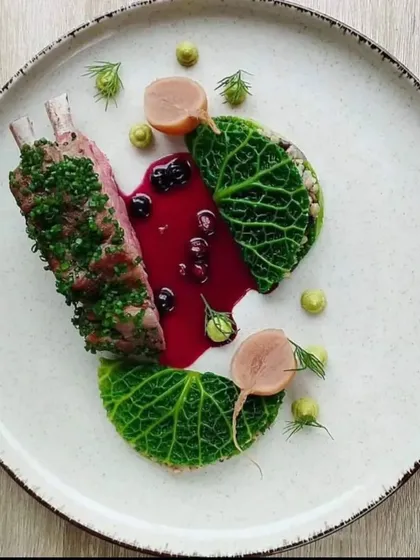 A rack of lamb, perfectly cooked and artfully plated. The dish is complemented by a rich berry reduction, savoy cabbage leaves, and dots of pea puree, demonstrating our capability for high-end cuisine.