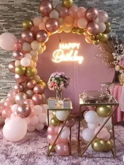 A beautiful home birthday setup with a circular pink backdrop, a rose gold and pink balloon arch, and elegant dessert stands.